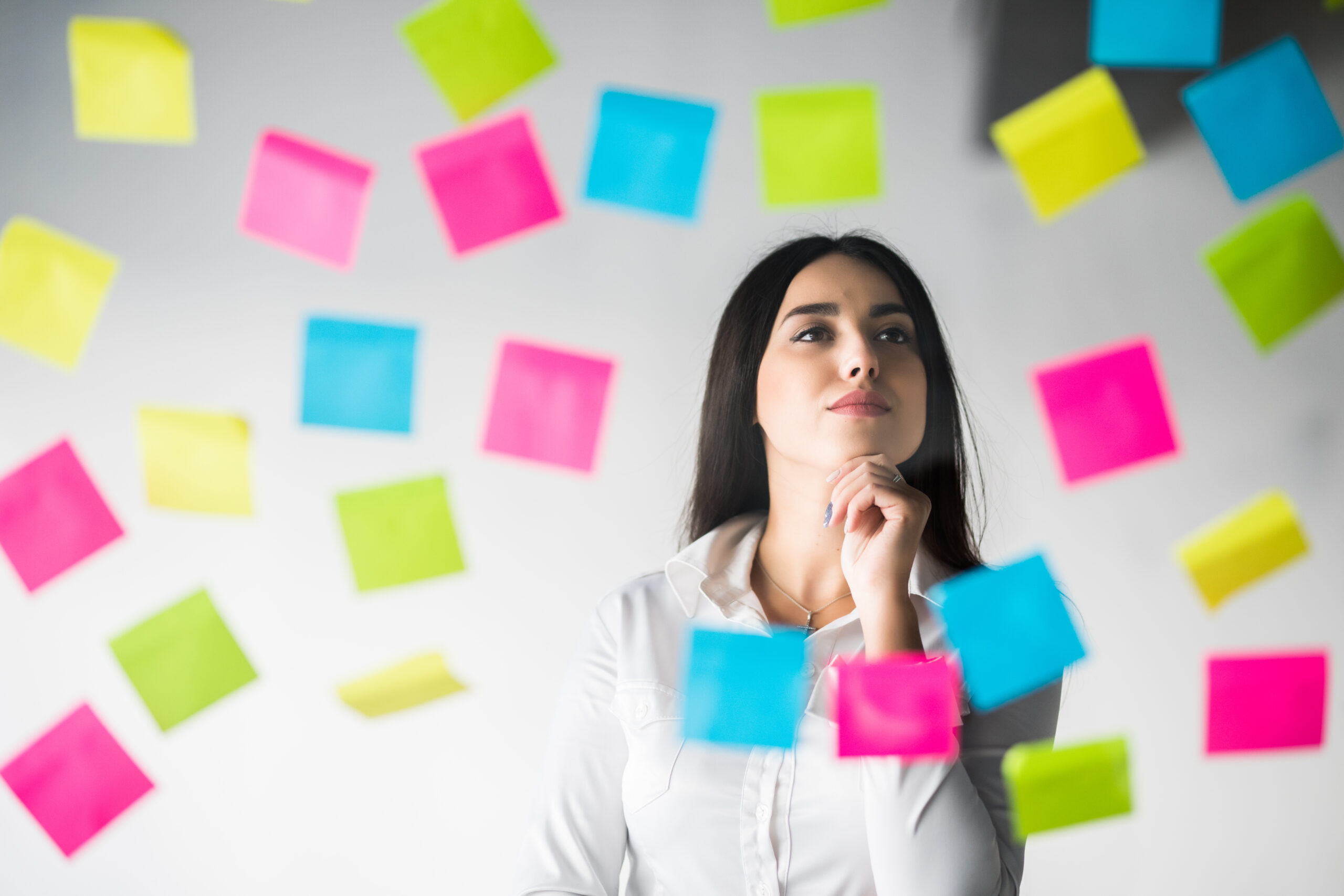 Mulher em ambiente de trabalho refletindo sobre um projeto com anotações e post-its