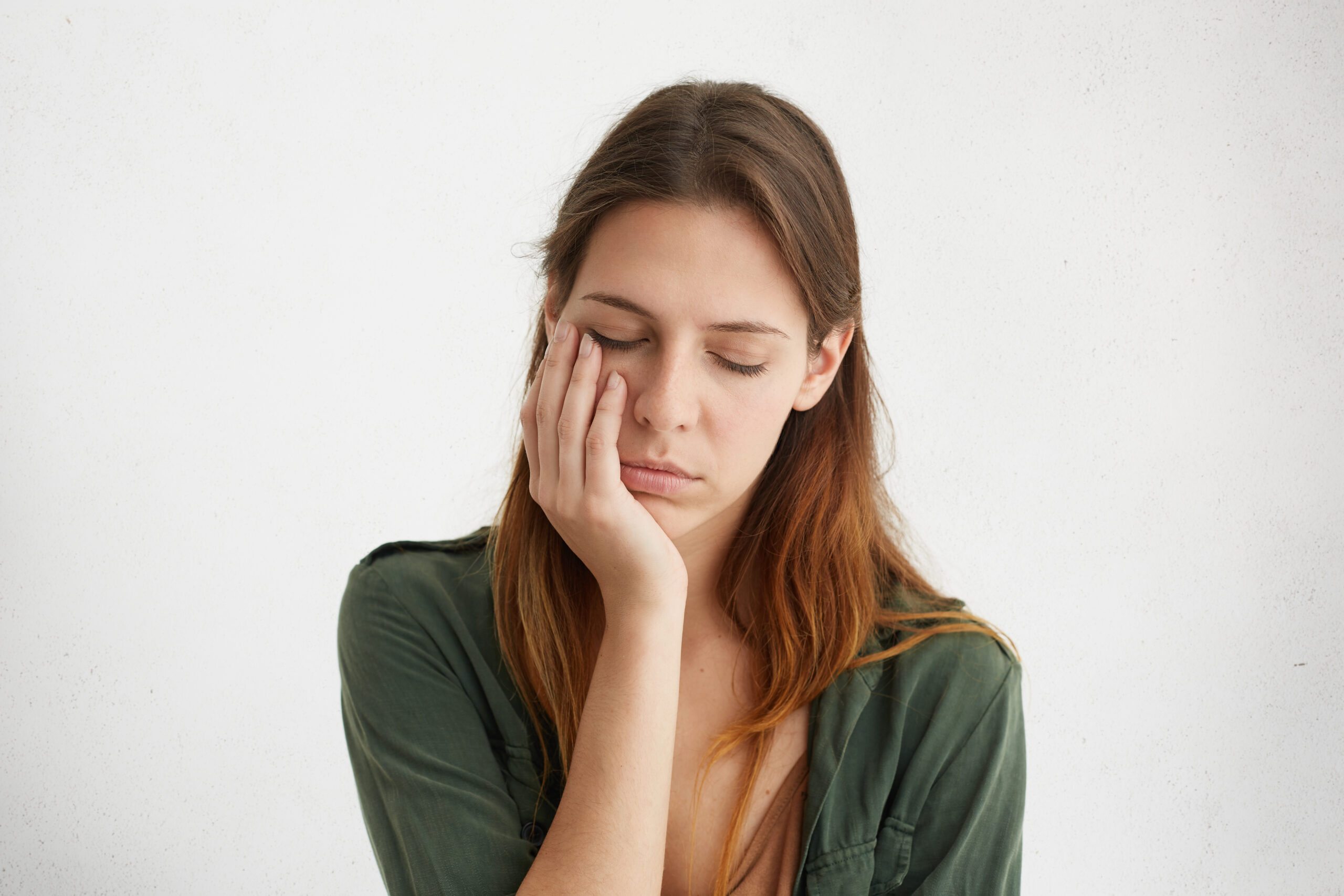 Mulher com expressão de cansaço, apoiando a mão no rosto e mantendo os olhos fechados
